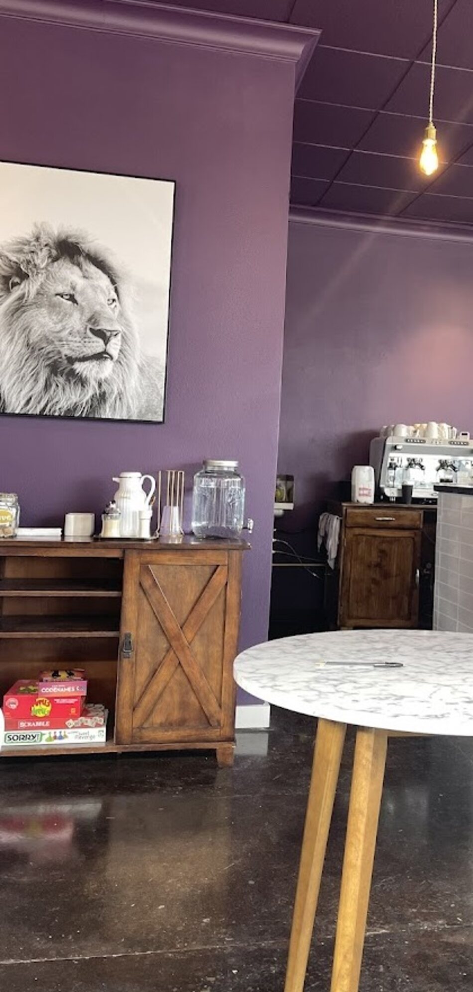 A corner of Kingdom Koffee with the lion portrait, a wood cabinet, and board games including Sorry! and Codenames on the shelf.